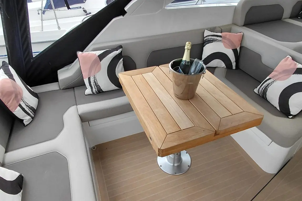 Elegant boat seating area with plush cushions, a wooden table, and a champagne bucket, offering a luxurious waterfront ambiance.